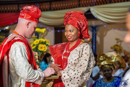 groom putting engagement ring on yoruba bride red white aso oke